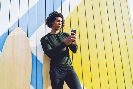 Thoughtful man with smartphone leaning on colorful plank wall
