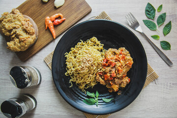 Flat lay, top view. Fried instant noodles with chicken spicy on the black plate and fried chicken on wooden board on wooden table