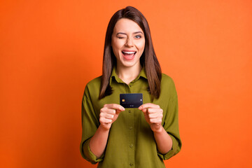 Photo of flirty excited girl presenting credit card close wink eye wear green shirt isolated orange color background