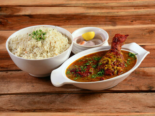 Traditional Indian cuisine, chicken curry and boiled rice on white ceramic bowl on the rustic wooden background, with lemon and onion