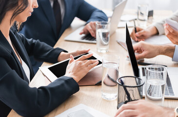 Cropped view of businesswoman using digital tablet near colleagues with devices and papers on...