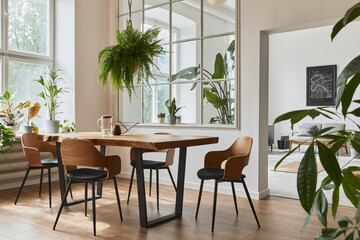 Stylish and cozy interior of dining room with design craft wooden table, chairs, plants, velvet...