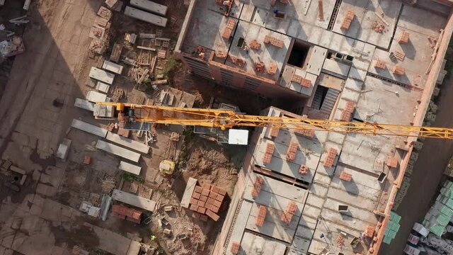 Aerial top view of a tower crane working on a building. There are workers in heavy engineering and construction. Construction site. High quality 4k footage