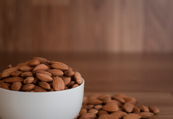 Almonds are in a white cup And all on the wood floor, Close up