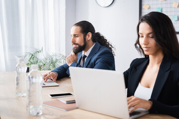 Hispanic businessman using laptop near smartphone and colleague at working table