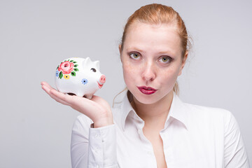 Fototapeta na wymiar Young red haired woman presenting a piggy bank / porcelain bank in her hand