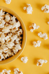 Popcorn in a yellow bowl on a yellow background. Top view. Copy, empty space for text
