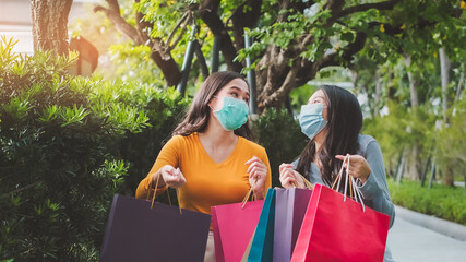 Asian woman wearing face mask. Happy woman with shopping bags enjoying in shopping. Girl holding colour paper bag.Friends walking in shopping mall.time shopping coronavirus crisis or covid19 outbreak.