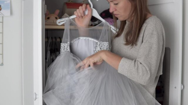 Mom puts things in the closet of a little girl. A woman pulls out a lush beautiful dress to celebrate baby's Christmas