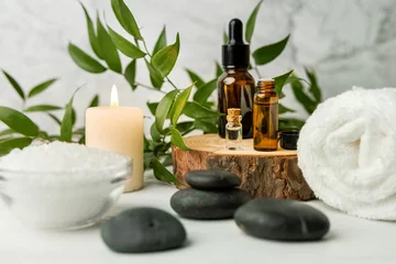 Photo sur Plexiglas Salon de massage articles de soins de beauté pour les procédures de spa sur une table en bois blanche avec une plante verte. pierres de massage, huiles essentielles et sel de mer avec bougie allumée