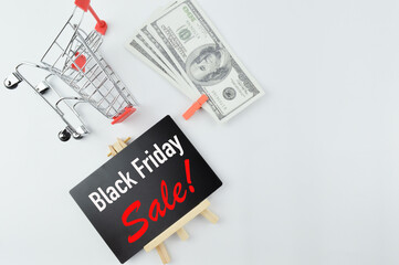Selective focus of shopping cart, banknotes and blackboard written with text BLACK FRIDAY SALE. Shopping concept.