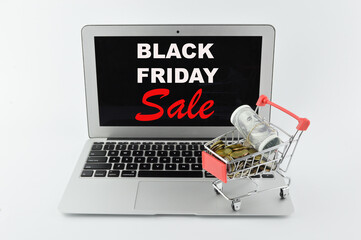 Selective focus of banknote, coins, shopping cart and laptop written with text BLACK FRIDAY SALE. Business concept.