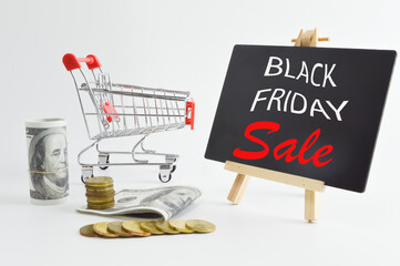 Selective focus of banknotes, stack of coins, shopping cart and blackboard written with text BLACK FRIDAY SALE. Shopping concept.
