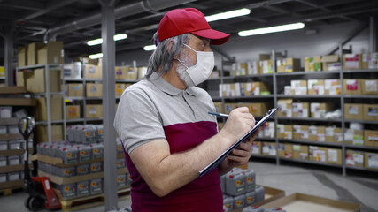 Aged male worker or supervisor with clipboard in safety mask at warehouse