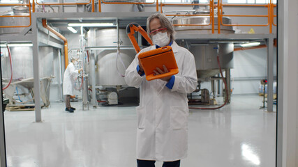 Mature engineer wearing lab coat and using tablet at chemical production plant
