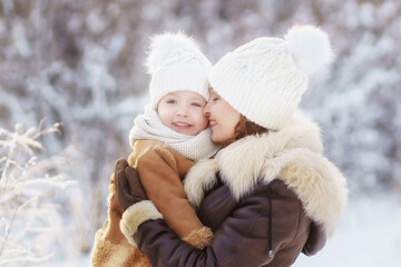 Fototapeta premium mother and daughter in brown fur coats hug during a walk through the winter forest. lots of snow around. bright emotion.