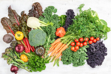 Variety of organic vegetables broccoli cauliflower carrots tomatoes kale pak choy onions. Healthy local farm produce on white wooden table, top view, selective focus