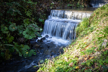 Obraz premium A mountain brook in late autumn. Small stream with waterfall captured in motion blur.