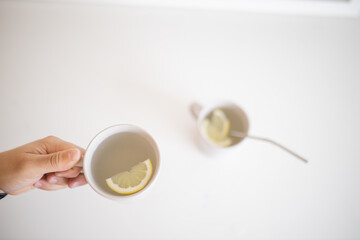 Obraz na płótnie Canvas Hand holding a cup of lemon tea with a lemon slice inside