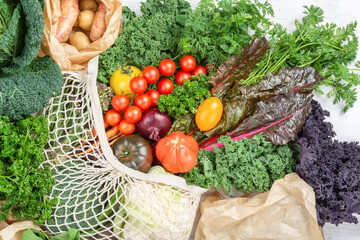 Eco shopping concept, colorful vegetables broccoli cauliflower carrots tomatoes kale pak choy chard in net and paper bags. Healthy local farm produce on white wooden table, top view, selective focus