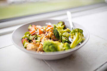 Broccoli and chicken salad on white bowl next to a window