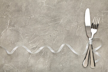 Christmas table place setting on grey background. Knife and fork with silver ribbon on grey