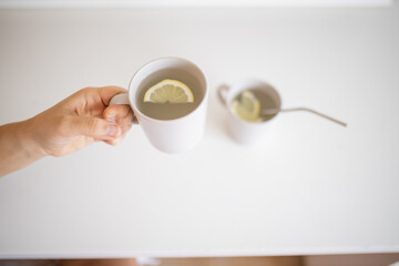 Hand holding a cup of lemon tea with a lemon slice inside