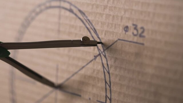 Man draws a circle with a compass on cardboard.