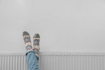 Woman warming legs on heating radiator near white wall, closeup. Space for text