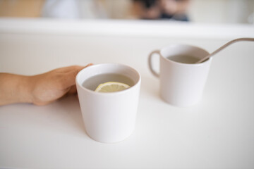 Hand holding a cup of lemon tea with a lemon slice inside