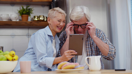 Mature couple using tablet computer surfing internet while having breakfast