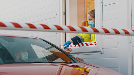 Worker in booth wearing protective mask and gloves checking temperature of male driver