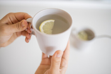 Hands holding a cup of lemon tea with a lemon slice inside