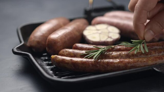 A girl puts rosemary on sausages and sausages in a grill pan, the camera moves to the side, close-up