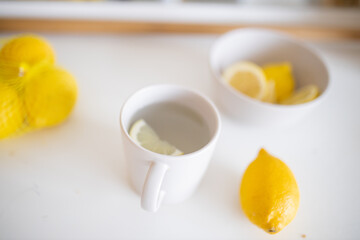 Cup of lemon tea on a white table surrounded by lemons