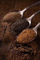 mix of seeds on spoons on wooden table. details of flax, chia and sesame seeds