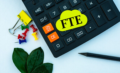 FTE - word on yellow note sheet on white background with calculator, pencil, green sheet and paper...