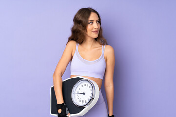 Young sport woman over isolated purple background with weighing machine