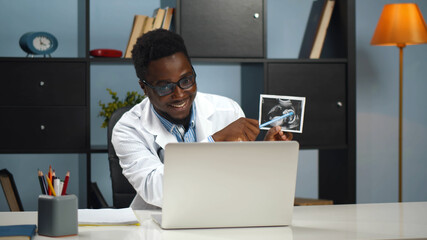 Black doctor showing sonogram image to patient on online conference