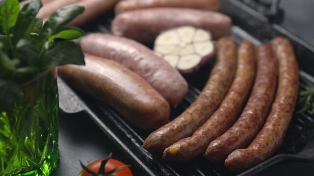 Sausages, sausages and tomatoes on a grill pan, dark background, the camera moves forward. Close-up