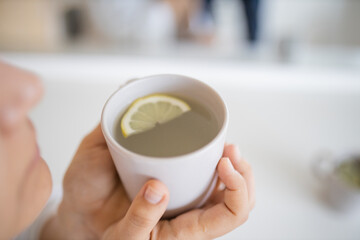 Woman gently blowing on a cup of lemon tea with a lemon slice inside