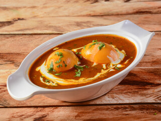 Anda Masala or Egg Curry is popular indian spicy food, served in a ceramic bowl over rustic wooden background. Selective focus