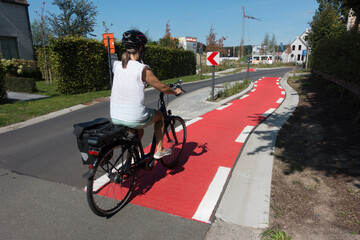 A female cyclist cycles on a dedicated cyle lane which is painted red and runs next to a road.She...