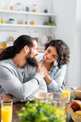 Smiling hispanic woman hugging husband near breakfast on blurred foreground