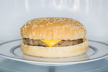 Microwavable cheese burger in a sesame seed bun in a microwave oven an example of modern fast food