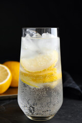 Soda water with lemon slices and ice cubes on black table
