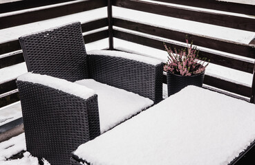 Close up view of snowy synthetic plastic rattan and glass garden furniture on cold winter day....