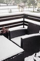 Close up view of snowy synthetic plastic rattan and glass garden furniture on cold winter day. Garden furniture maintenance concept.