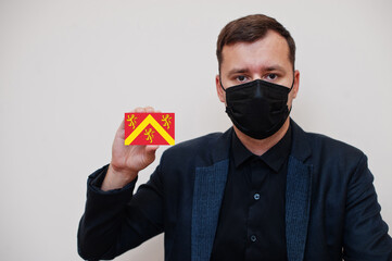 Man wear black formal and protect face mask, hold Anglesey flag card isolated on white background. United Kingdom counties of Wales coronavirus Covid concept.