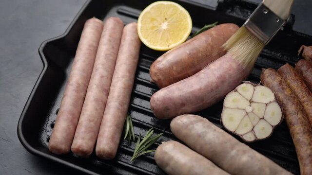 outputA girl greases grilled sausages with butter on a grill pan with lemon, rosemary and garlic. Close-up. The camera moves to the side